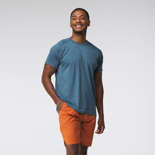 A person in an NRS Silkweight Short-Sleeve Shirt - Men's, moisture-wicking and blue, paired with orange shorts, smiles against a plain background.