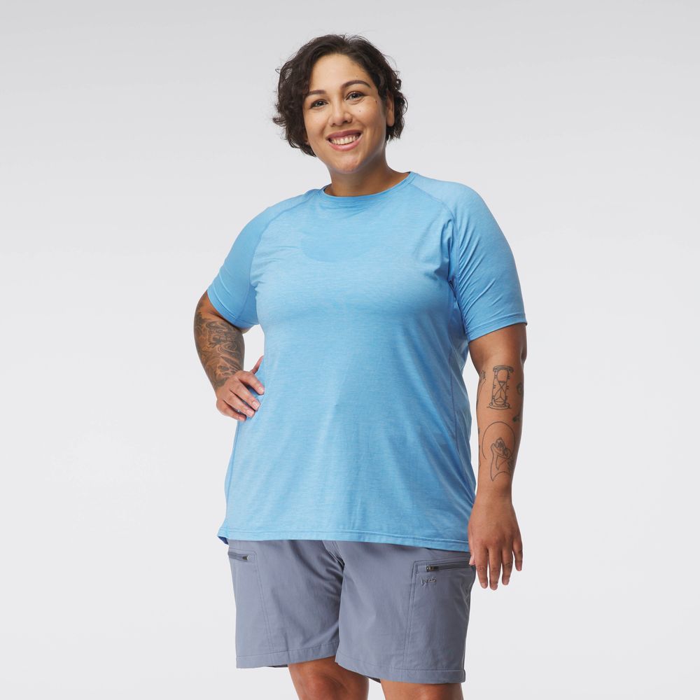 A woman in an NRS Silkweight Short Sleeve Shirt stands smiling against a white backdrop, with one hand on her hip. The light blue t-shirt and gray shorts offer excellent breathability, perfect for staying cool and comfortable all day long.