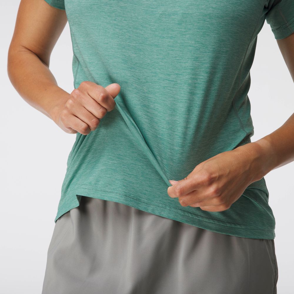 A woman in a green Silkweight Short Sleeve NRS shirt with moisture-wicking fabric and gray pants pulls on the hem of the shirt.