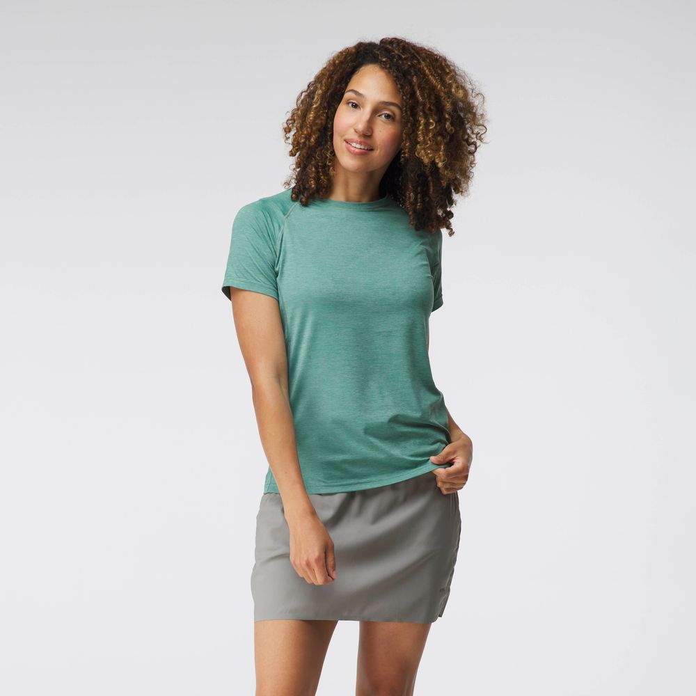 A woman in a NRS Silkweight Short Sleeve Shirt and a gray skirt stands against a plain background, appreciating the shirt's breathability.