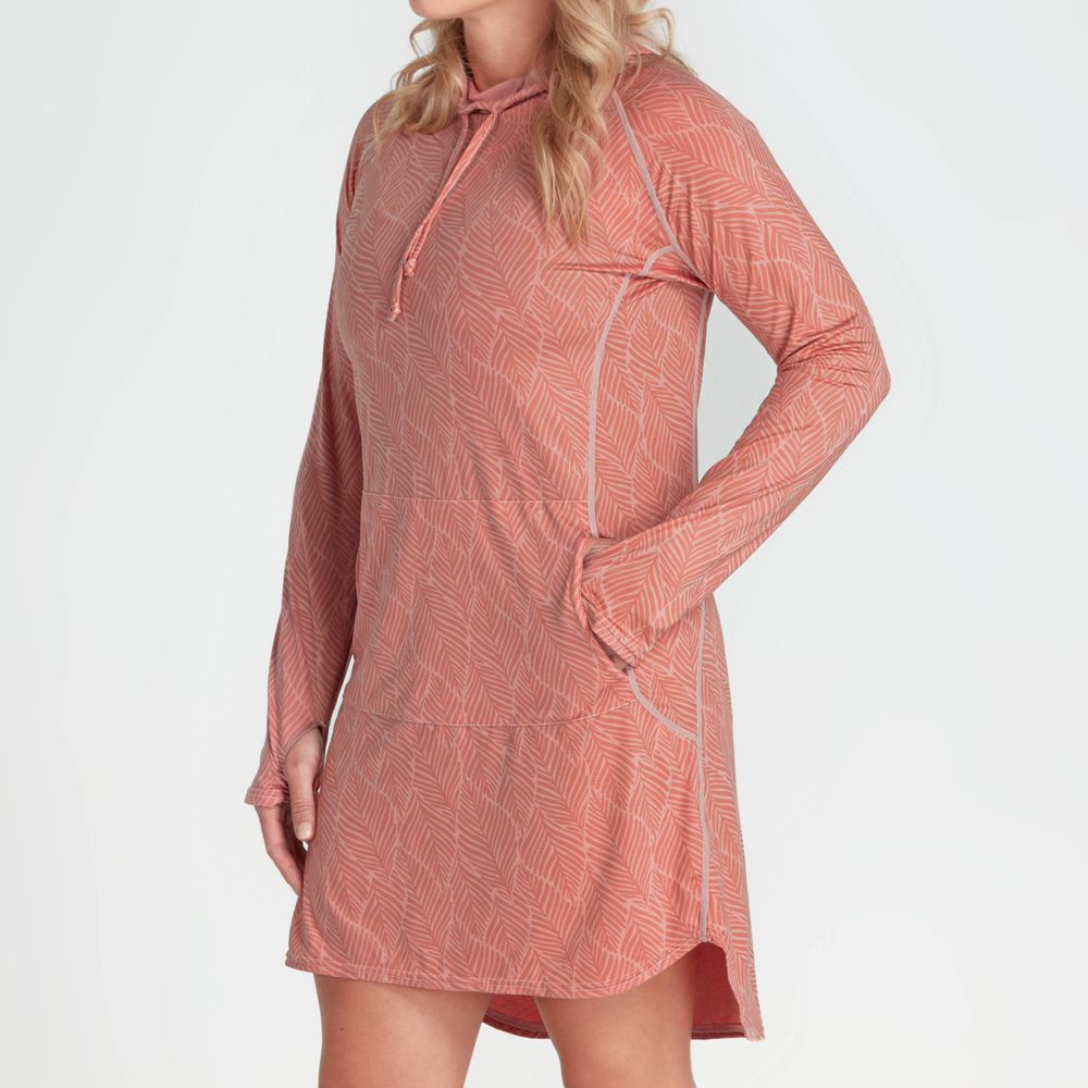 The person is wearing an NRS Silkweight Hoodie Dress in a coral pattern that offers sun protection, made from recycled materials for an eco-friendly yet stylish and functional piece.