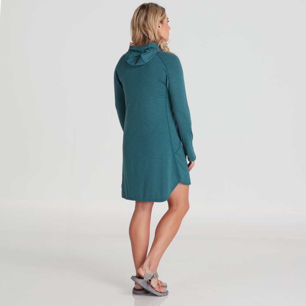 A woman in an NRS Silkweight Hoodie Dress, crafted from recycled material, faces away against a plain gray backdrop, with sandals finishing her look.