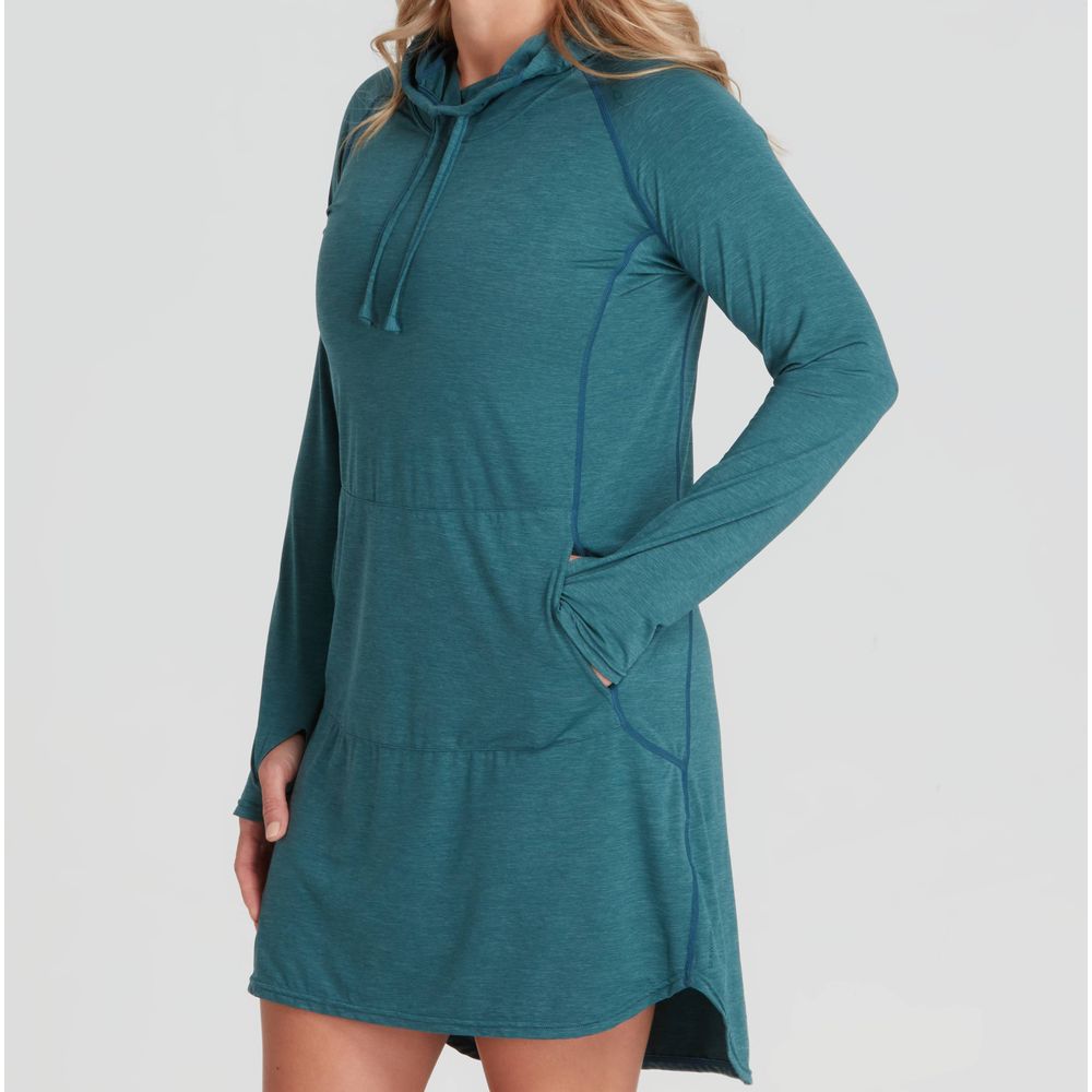 A person models the NRS Silkweight Hoodie Dress, crafted from recycled materials in a teal long-sleeve design with pockets, providing style and sun protection against a plain backdrop.