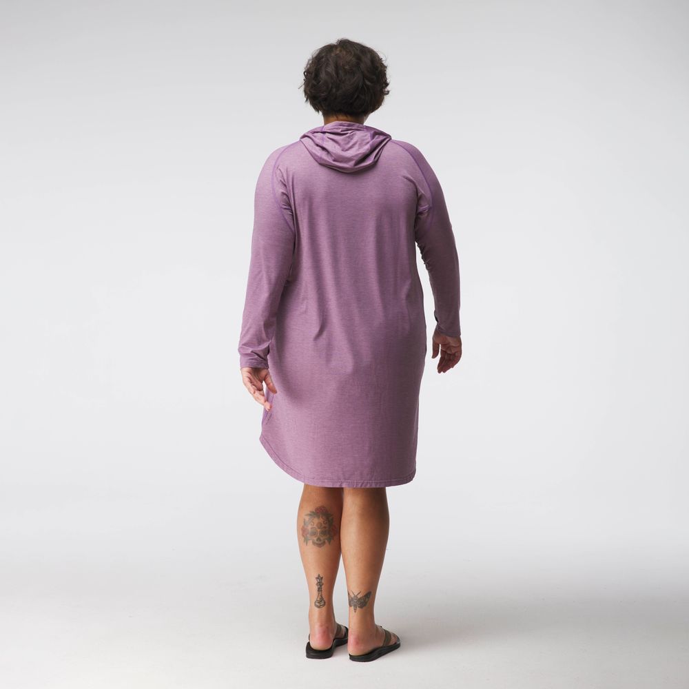 Facing away, a person with short hair wears an NRS Silkweight Hoodie Dress in purple paired with black sandals, revealing tattoos on both legs. Made from recycled materials, the dress combines style with eco-friendliness against a plain white background.
