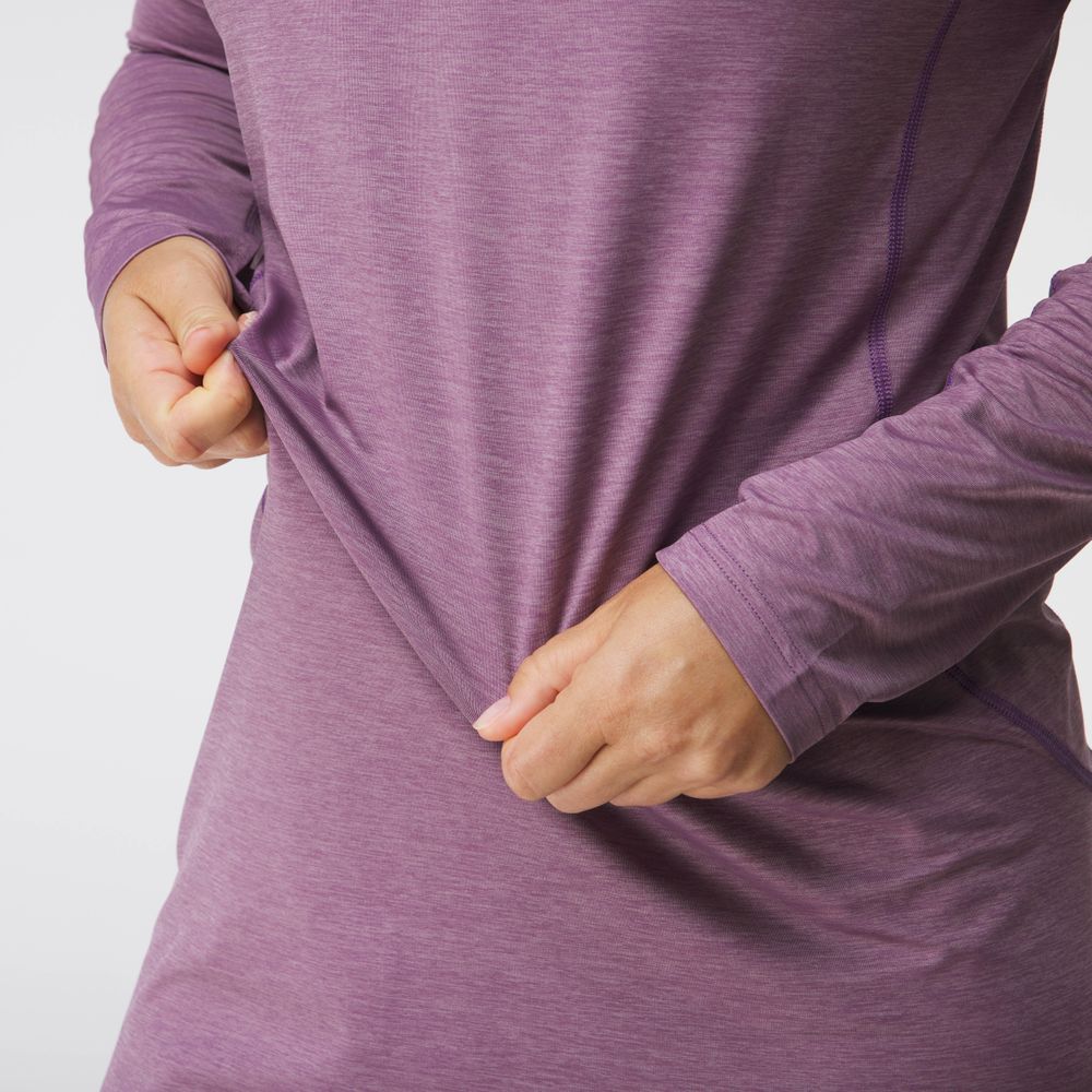 A person wears an NRS Silkweight Hoodie Dress, a long-sleeved purple top made from recycled materials, gently pulling the fabric from the side against a plain background.
