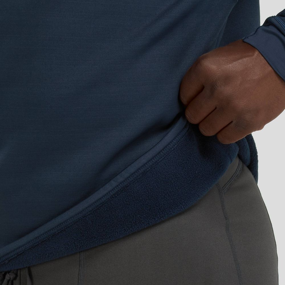The person is adjusting a NRS Expedition Weight Shirt - Men's in dark blue, creating a stylish layered look. Combined with gray pants, this outfit uses recycled fleece and offers UPF 50+ protection, merging fashion with function.