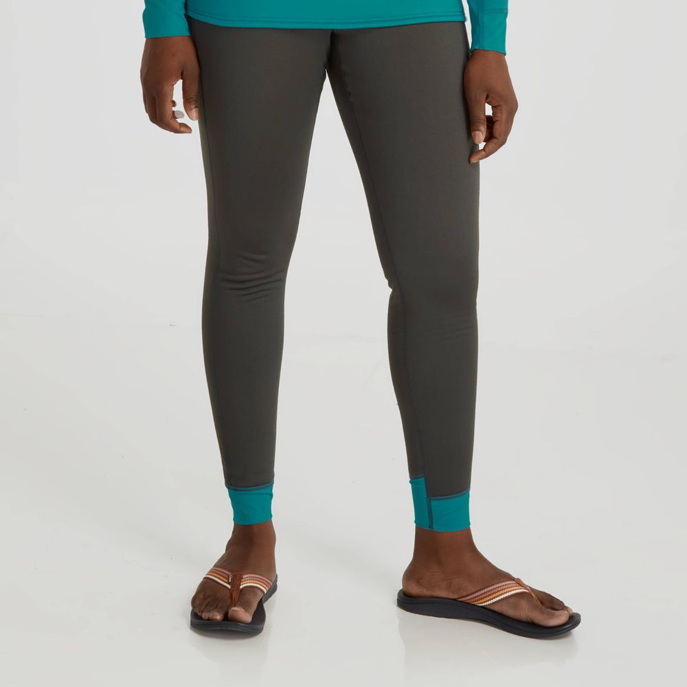 A person in NRS Expedition Weight Pants - Women's, a teal long-sleeve top, and striped-strap sandals stands on a white background.
