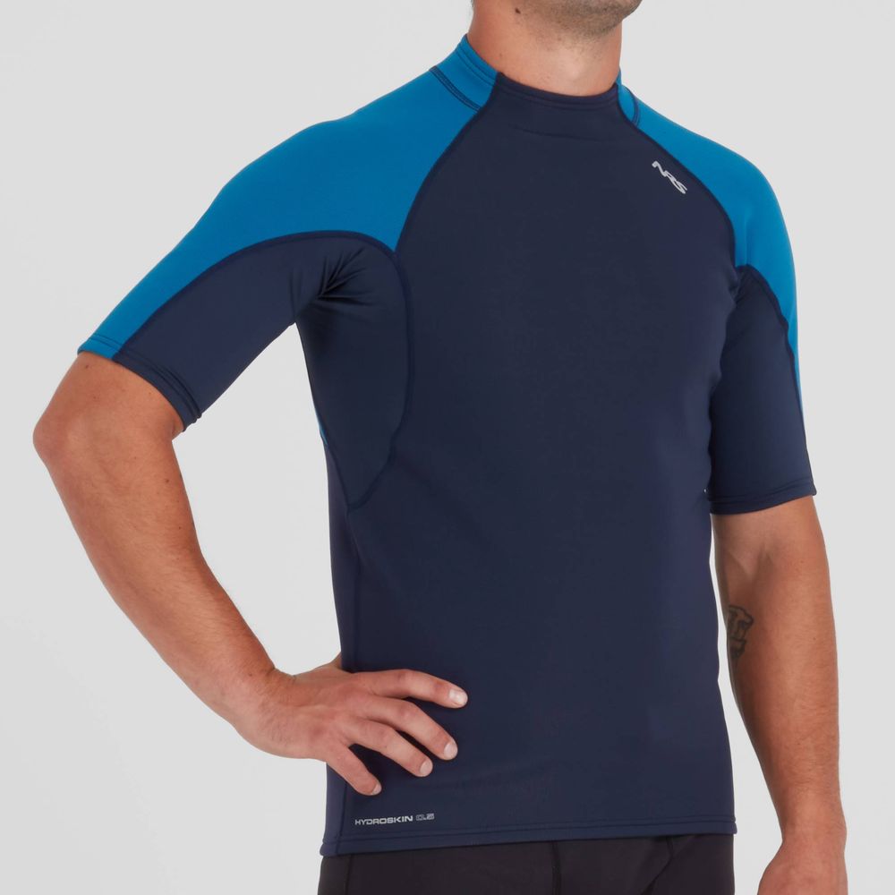 A person wearing an NRS Hydroskin 0.5mm Short Sleeve Shirt - Men's in navy and blue, crafted for peak paddling performance, stands against a plain background.