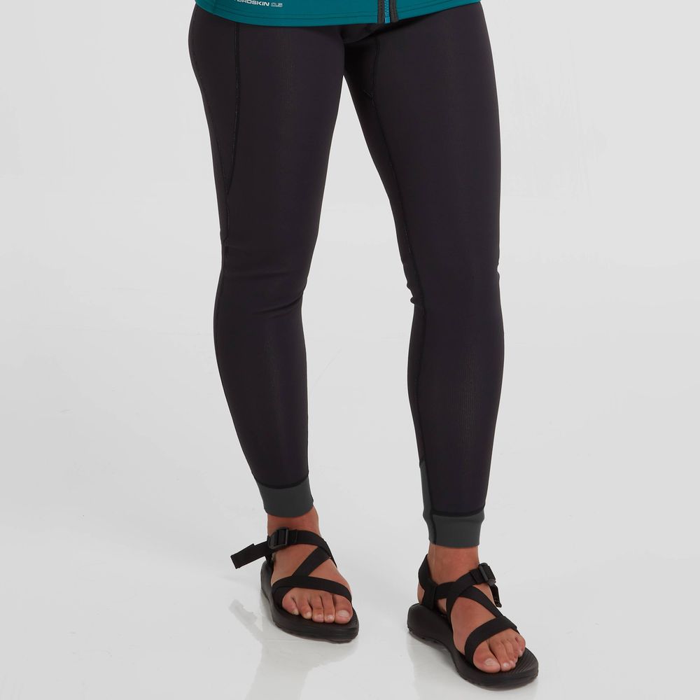 Wearing NRS Hydroskin 0.5mm Pant - Women's with black sandals, a person stands on a white background, appreciating the insulation offered by the sleek neoprene design.