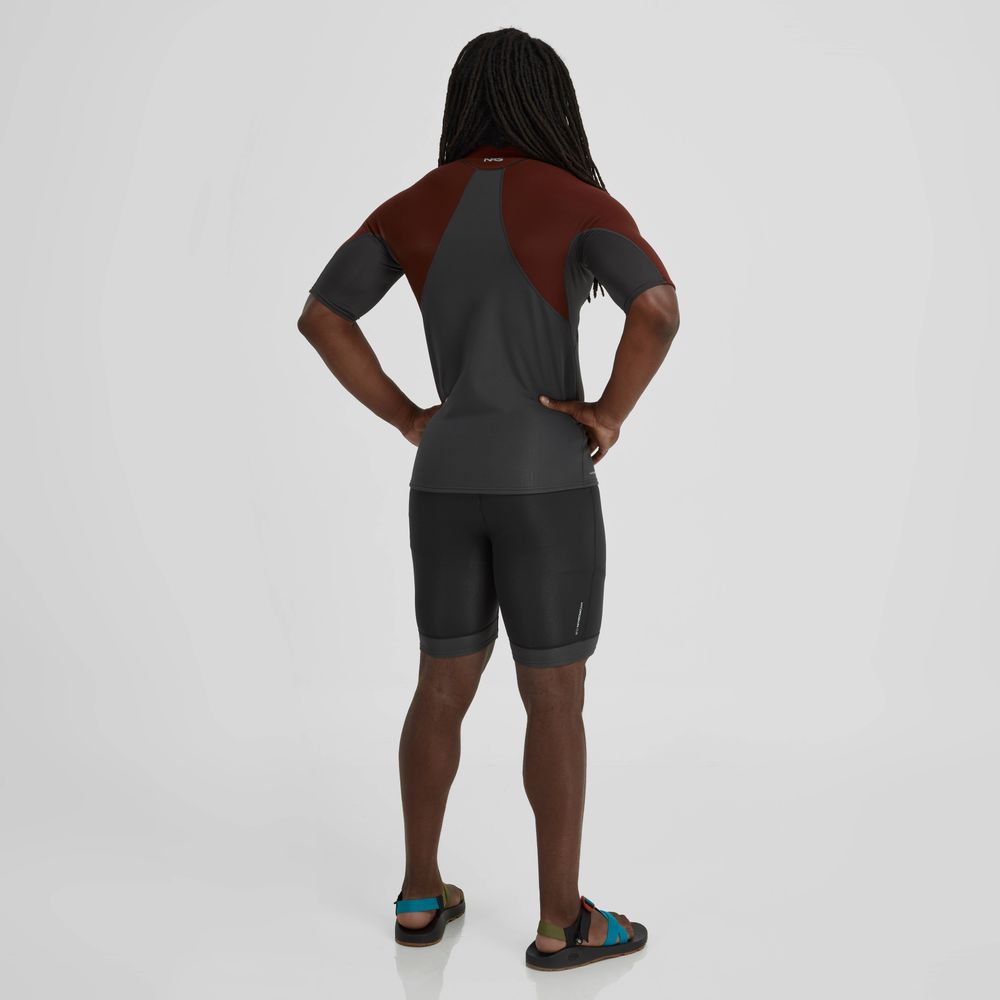 A person with long hair faces away from the camera, modeling NRS Hydroskin 0.5m Shorts for men and a short-sleeve cycling suit in black and brown neoprene, stylishly paired with sandals.