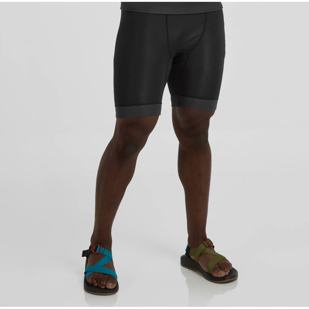 A person models sleek black NRS Hydroskin 0.5m Shorts - Men's, paired with vibrant neoprene sandals, against a plain background.