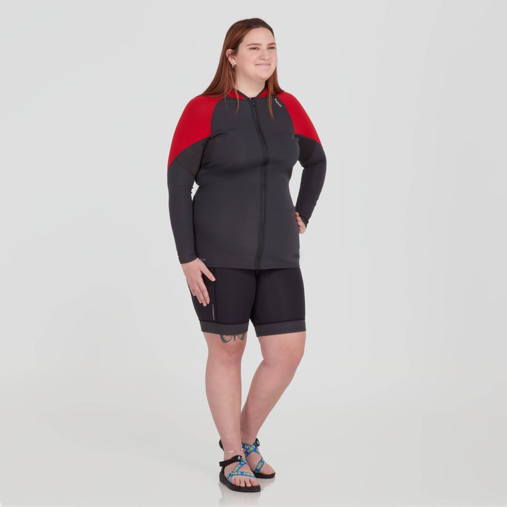 A person stands confidently with hands on hips, wearing NRS HydroSkin 0.5mm Shorts and sandals against a plain backdrop. Their outfit features advanced Terraprene neoprene, enhancing paddling performance for an optimal aquatic experience.