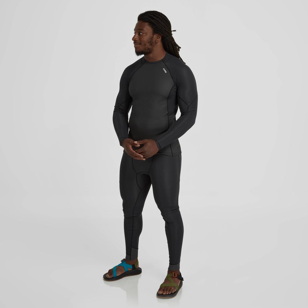 Wearing the NRS Hydroskin 1.0mm Long Sleeve Shirt and colorful sandals, a person poses against a white background, blending style with functionality for cold water adventures.