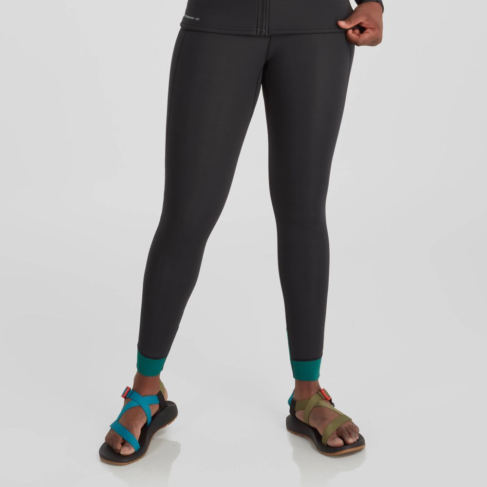 A person in NRS Hydroskin 1.5mm Women's Pants with teal cuffs and colorful sandals stands against a plain background, prepared for optimal paddling performance with neoprene insulation.