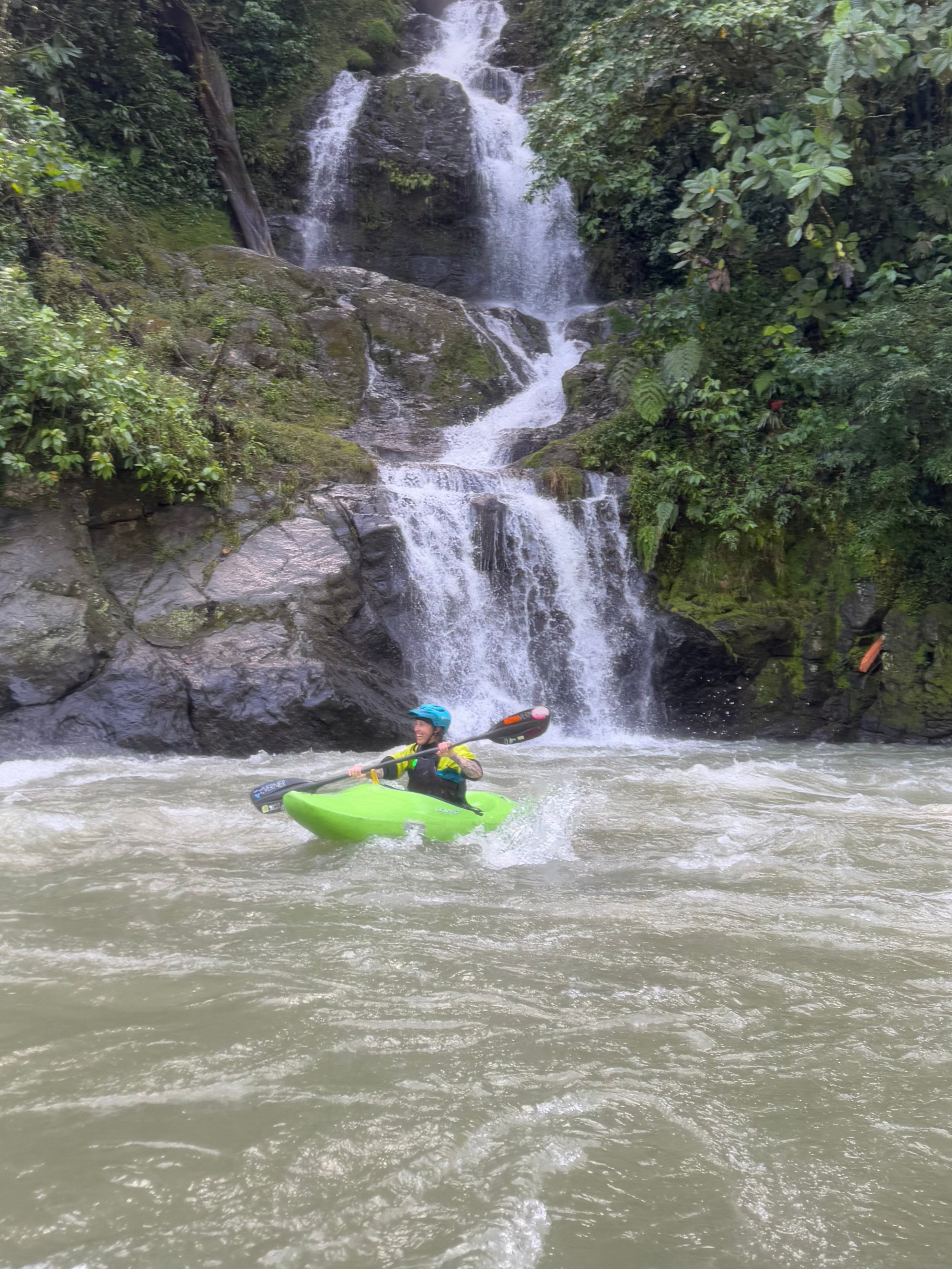 A woman paddles a green kayak by a waterfall in lush forest—a perfect setting for the Ladies Costa Rica Paddling Retreat by 4CRS Paddle School.