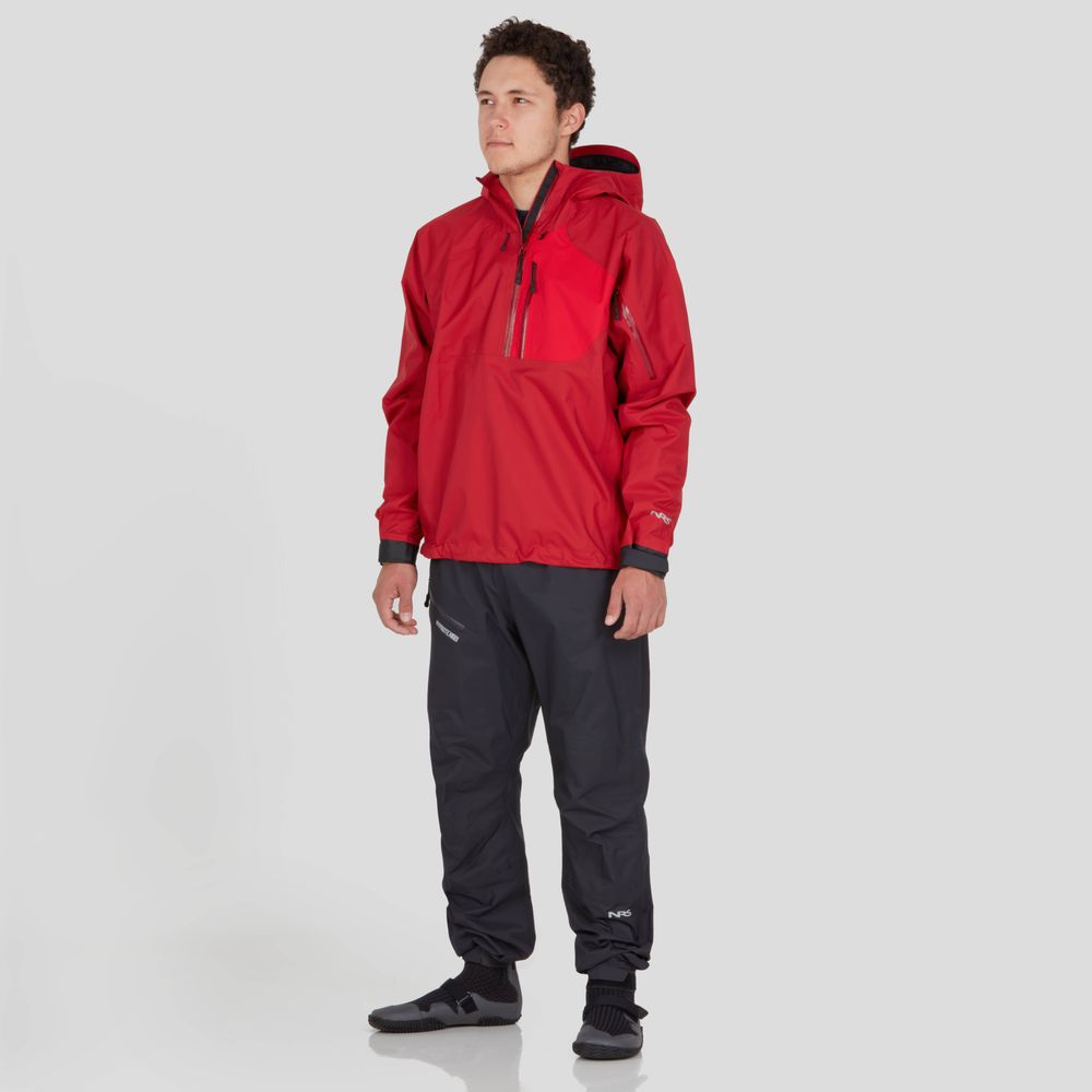 A person wearing the NRS High Tide Jacket for men in red, paired with black waterproof pants, stands against a plain white background.