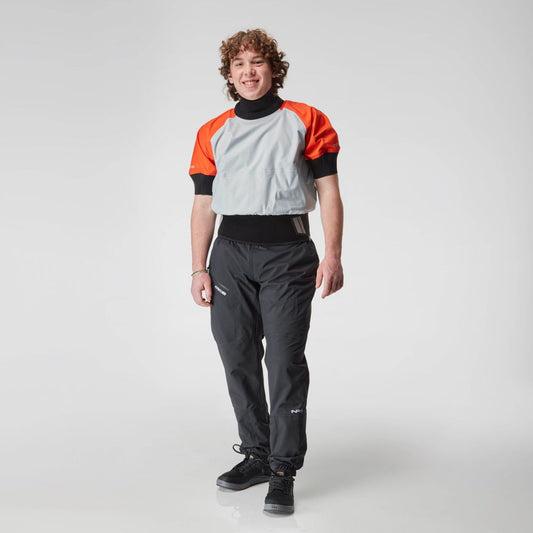 An individual wearing an orange and gray NRS Stratos Short Sleeve Paddling Jacket, paired with black pants and shoes, stands against a white background.