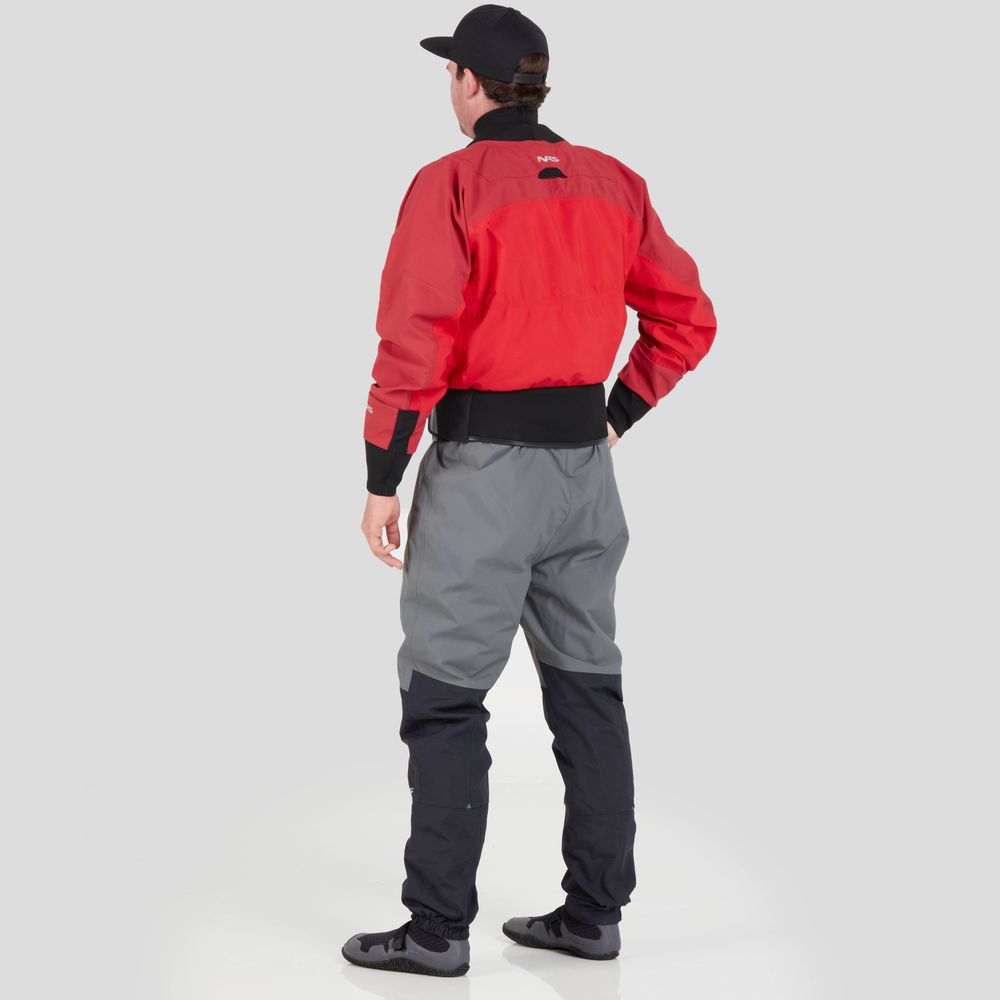 A person in a vibrant red NRS REV (GORE-TEX Pro) Drytop stands confidently with hands on hips, wearing gray pants and a black cap. Against the plain gray background, they exude readiness for any adventure, promising exceptional paddling performance in all conditions.