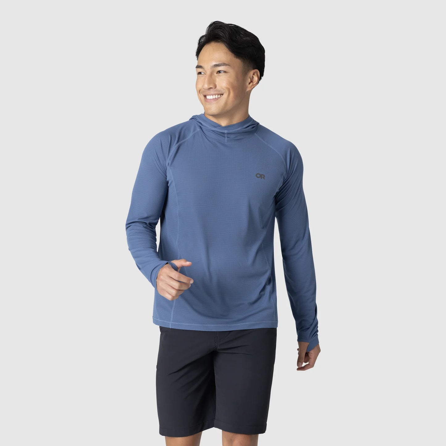 A man wears the Outdoor Research Echo Hoodie - Men's in blue and black shorts, standing against a plain light background, smiling and looking to the side.