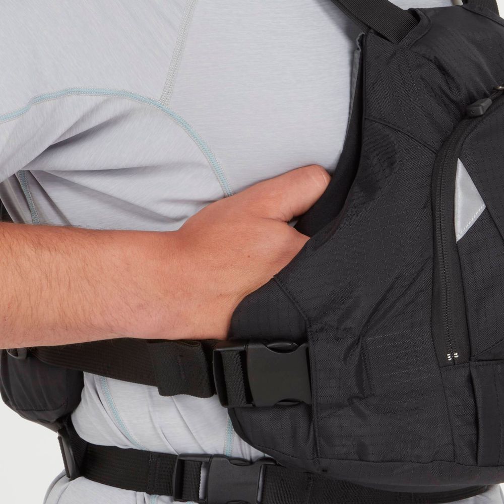 A person in a light gray shirt adjusts a black tactical vest with a clip buckle, similar to the secure fit of an NRS Ninja PFD.