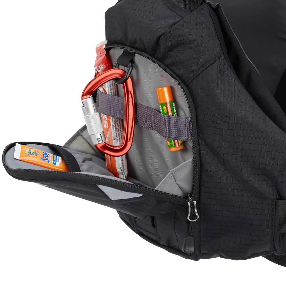 An NRS Ninja PFD backpack, partially open, reveals a red carabiner, sunscreen, lip balm, and a hint of an adventure-ready jacket tucked inside.