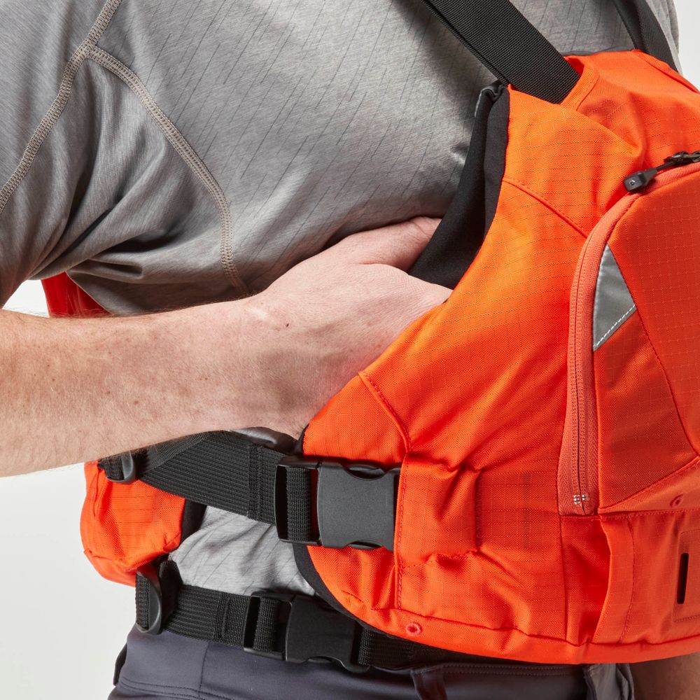 A person adjusts an NRS Ninja PFD, a bright orange life jacket with black straps, while wearing a gray shirt—offering paddlers flotation in a compact design.
