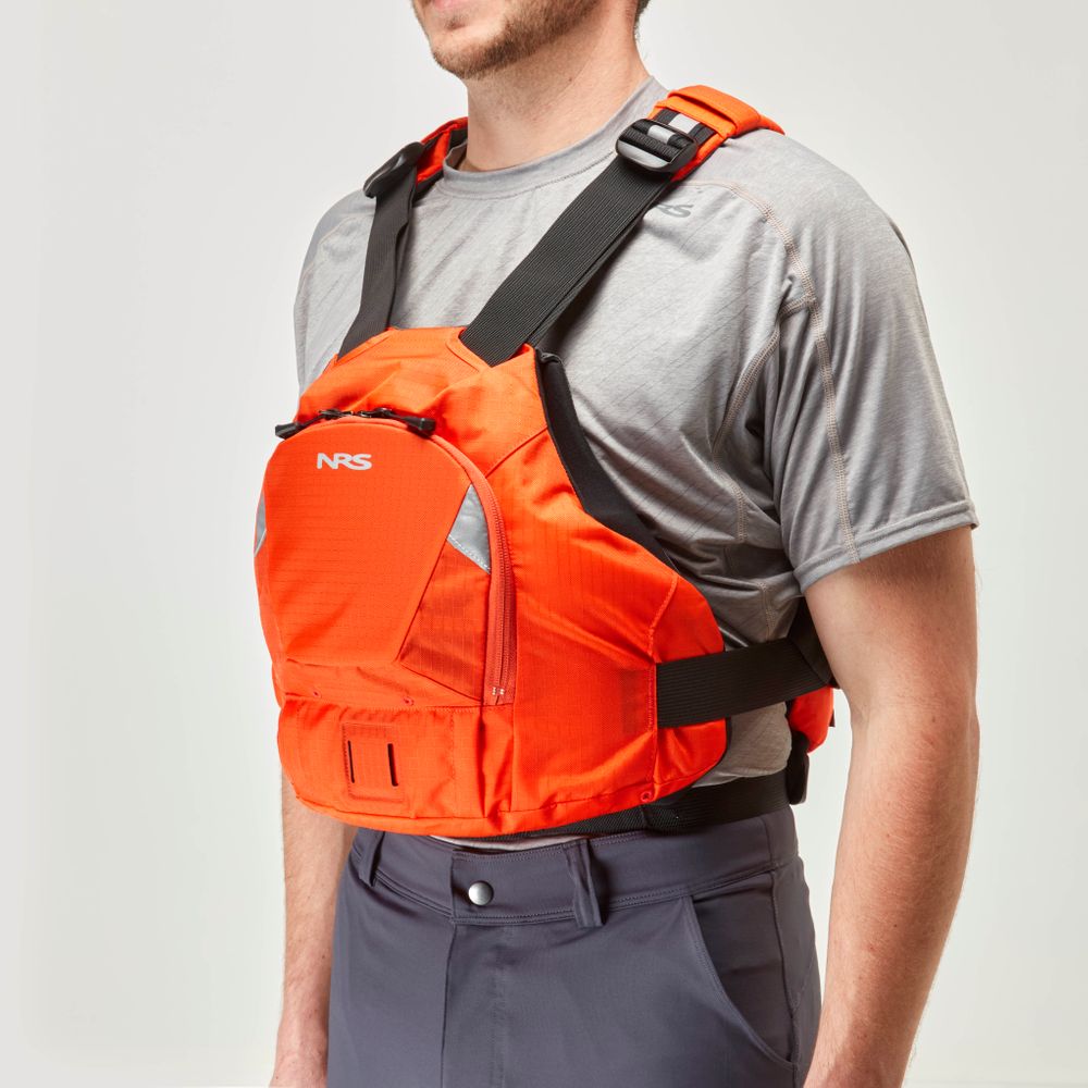 A person is wearing a gray shirt, dark pants, and an NRS Ninja PFD in orange, featuring a front zippered pocket, adjustable straps, and an orbit fit system for enhanced comfort.