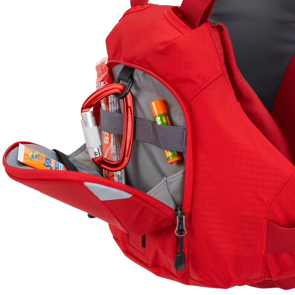 The red backpack has an open side pocket revealing essentials such as a carabiner, lip balm, sunscreen, and an energy bar. It's ideal for adventures or when used alongside the performance of the NRS Ninja PFD.