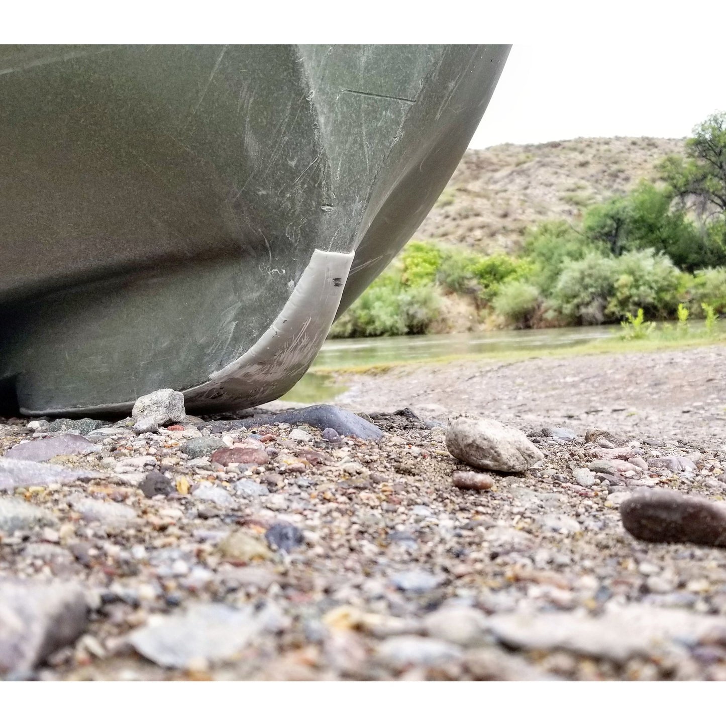 The bottom of a kayak with rocks on it, equipped with NRS Gator Guard Patch.