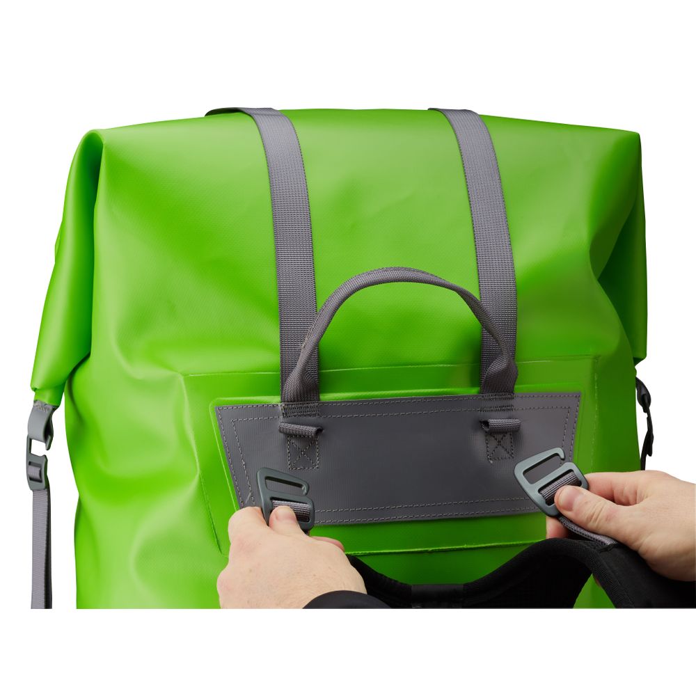 Hands adjusting the compression straps on a bright green NRS Bill's Bag waterproof backpack with dark gray accents.