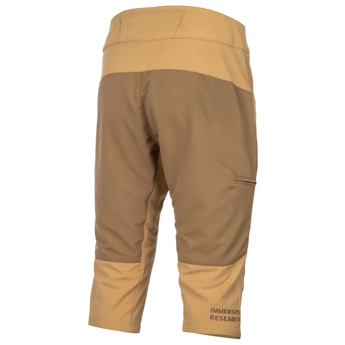 The Immersion Research Shinzer Shorts are tan and light brown knee-length outdoor shorts with a side pocket, articulated knees for improved movement, and "Immersion Research" printed near the left cuff, shown from the back.