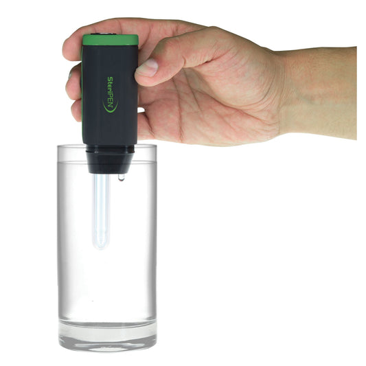 A hand holds a Katadyn SteriPen Adventurer Opti water purifier above a glass of water, preparing to use its UV light technology for purification.