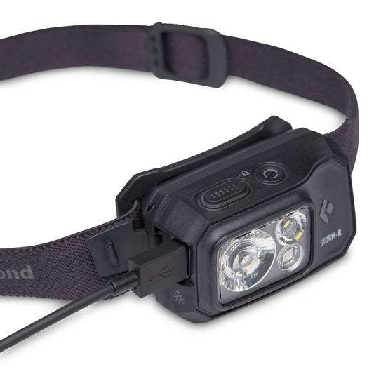 The Black Diamond Storm 500R Rechargeable Headlamp, featuring an adjustable strap, is shown being charged with a USB cable connected to its side.