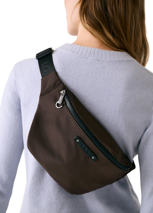 Someone wearing the Lole Taylor Belt Bag in brown, featuring a zippered pocket, over a light gray sweater, shown from the back.