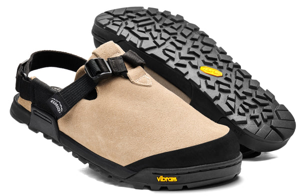 The Bedrock Mountain Clog is a tan suede outdoor sandal with black soles and adjustable straps, featuring a rugged Vibram Megagrip outsole for traction—an ideal camp shoe after long hikes.
