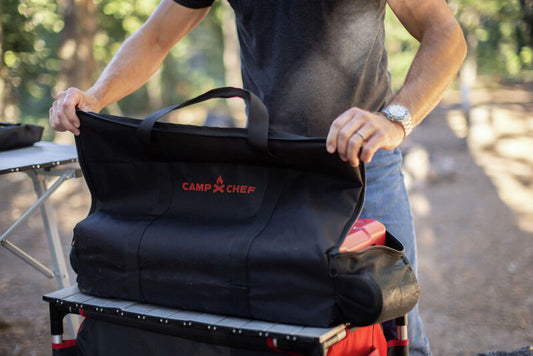 A man placing an Everest 2X Carry Bag on a cart in the woods made with durable fabric by Camp Chef.