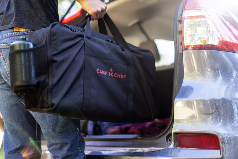 A man loading a Camp Chef Everest 2X Carry Bag into the trunk of a car.