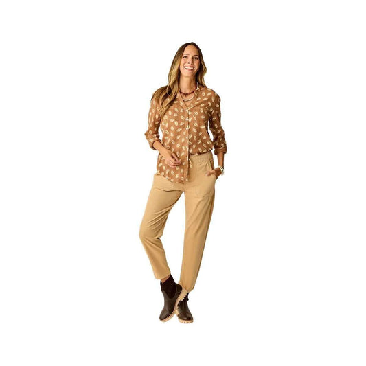 A woman smiles wearing the Carve Dylan Gauze Tunic—a versatile brown patterned blouse—paired with tan pants and brown ankle boots against a white background.