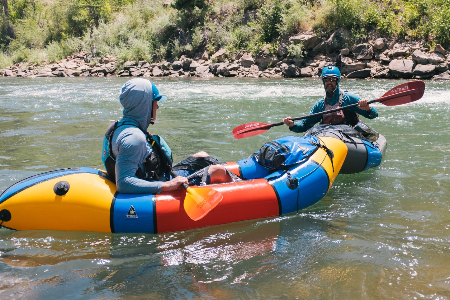Two young adults equipped with 4CRS Paddle School gear embark on an exhilarating river adventure in colorful inflatable kayaks, navigating through lush greenery while experiencing the excitement of the "Youth-Young Adult Level 1: Packrafting Foundations.