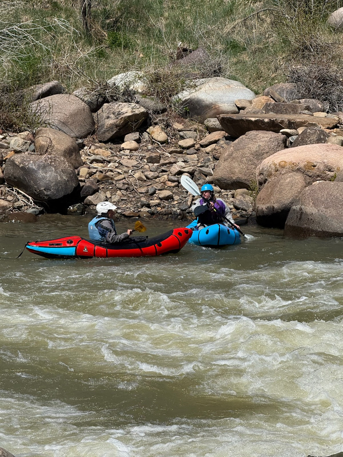 Two people wearing helmets paddle inflatable kayaks through rapids—an exciting look at the 4CRS Paddle School's Adult Intro to Packrafting course in action.