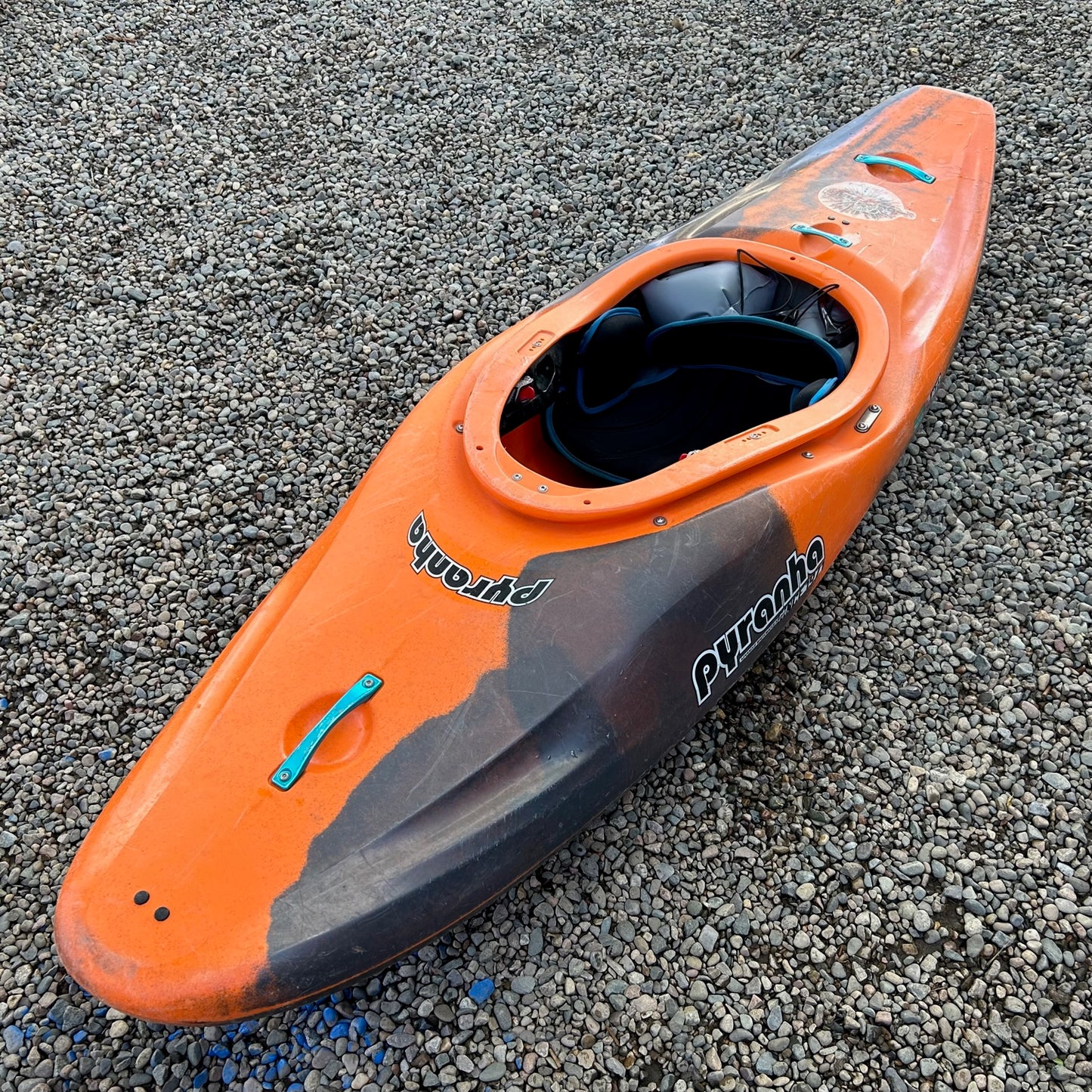 A Pyranha Demo Firecracker 242 kayak laying on the ground.