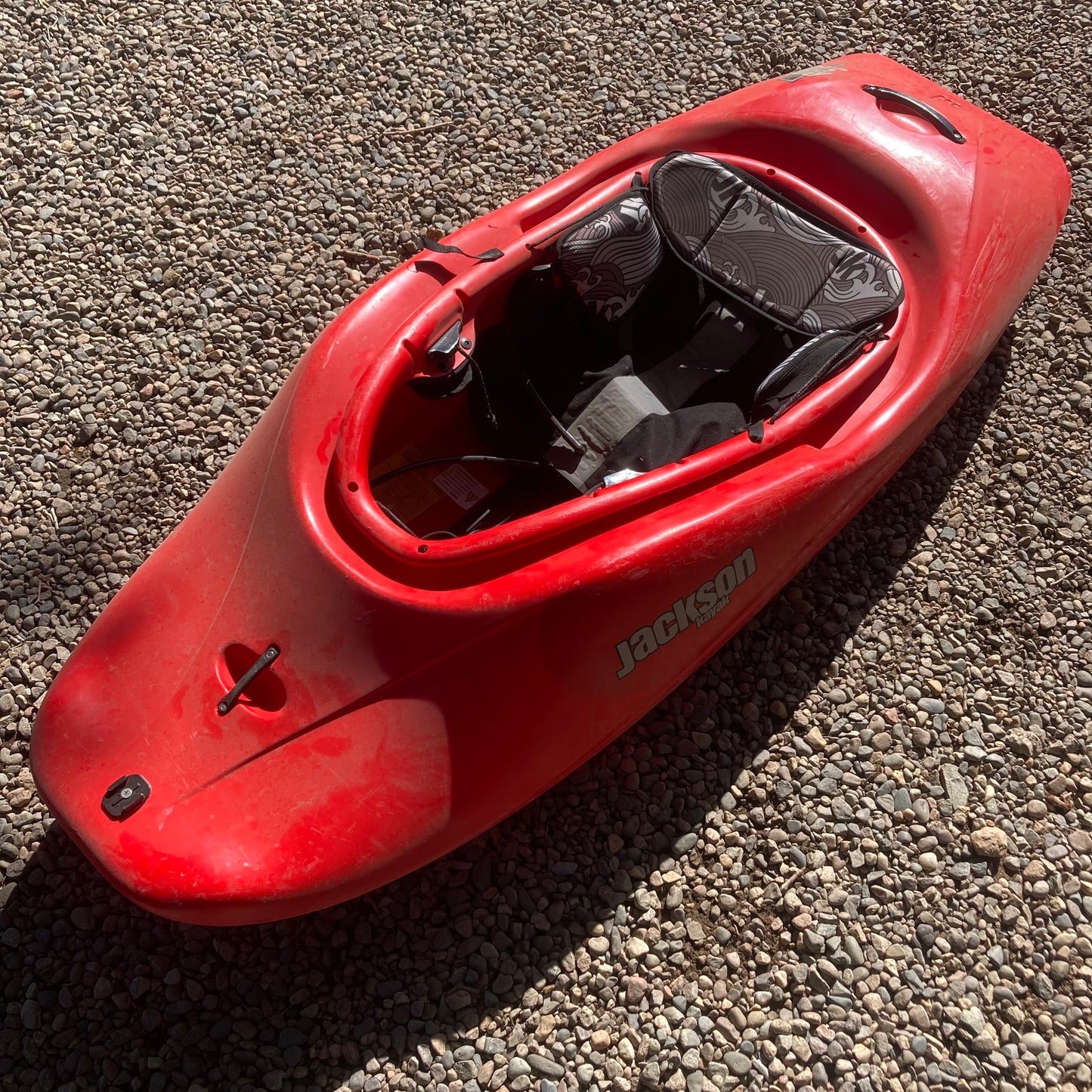 A red Jackson Kayak Demo Rockstar V MD sitting on gravel.
