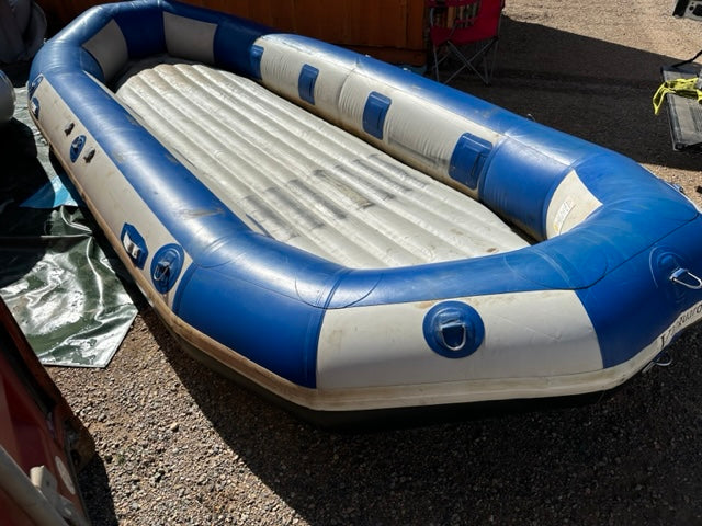 A used blue and white Used 16' Vanguard Raft, in fair condition, sitting in a parking lot.
