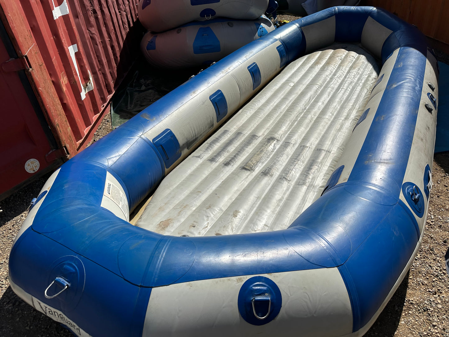 A used 16' Vanguard Raft by 4Corners Riversports, blue and white, sitting on the ground in fair condition.