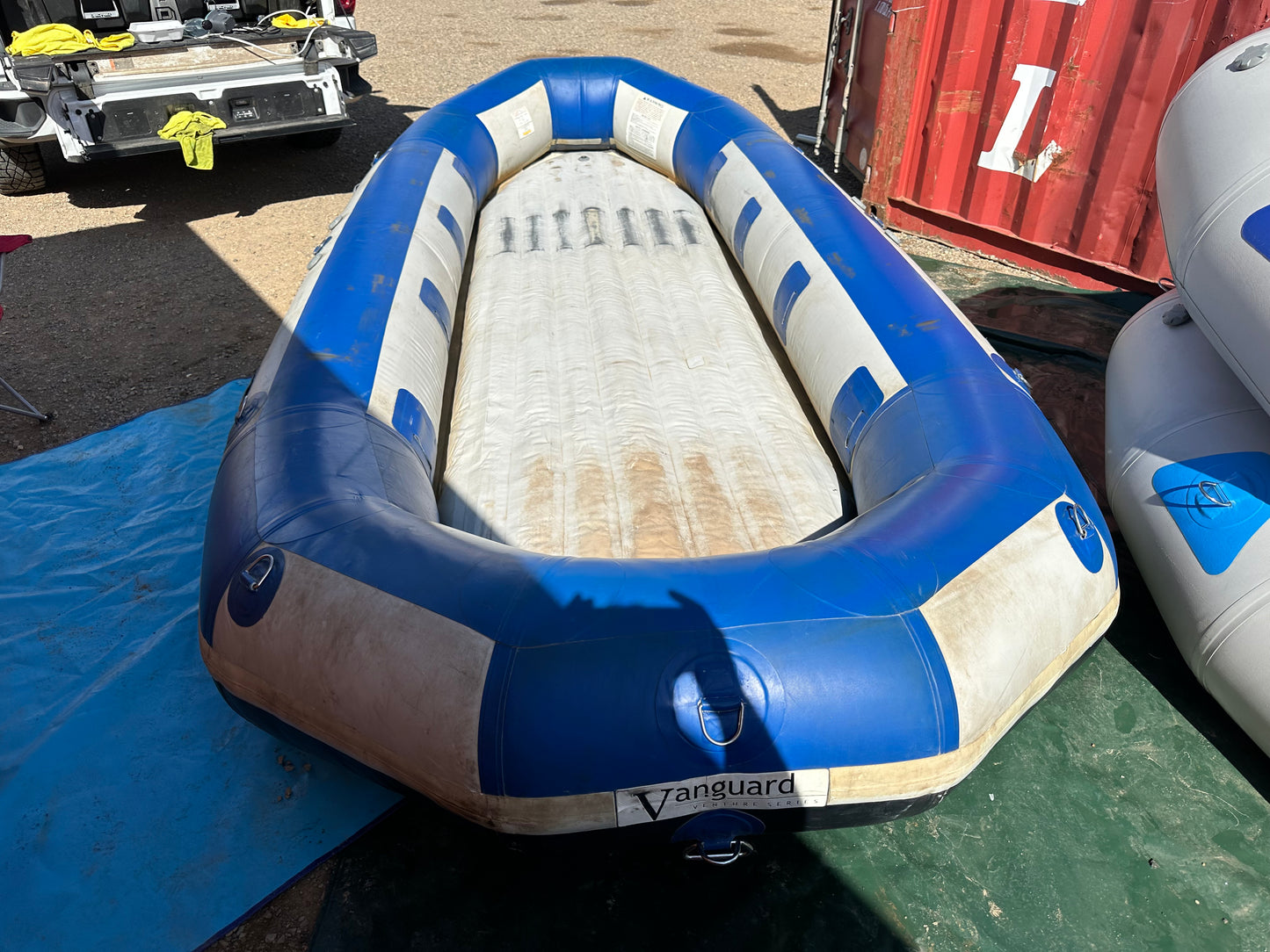 A used 16' Vanguard Raft in fair condition is sitting on the ground, displaying a blue and white color scheme.