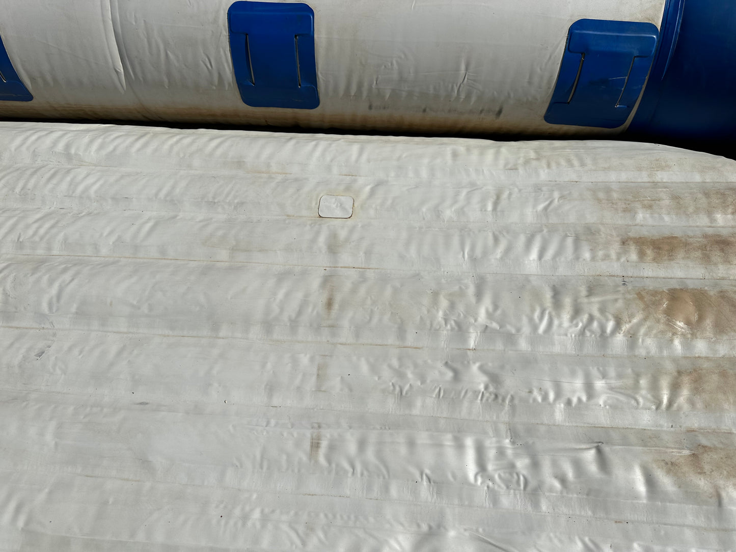 A white and blue Used 16' Vanguard Raft, maintained in fair condition, sitting on top of another tarp.