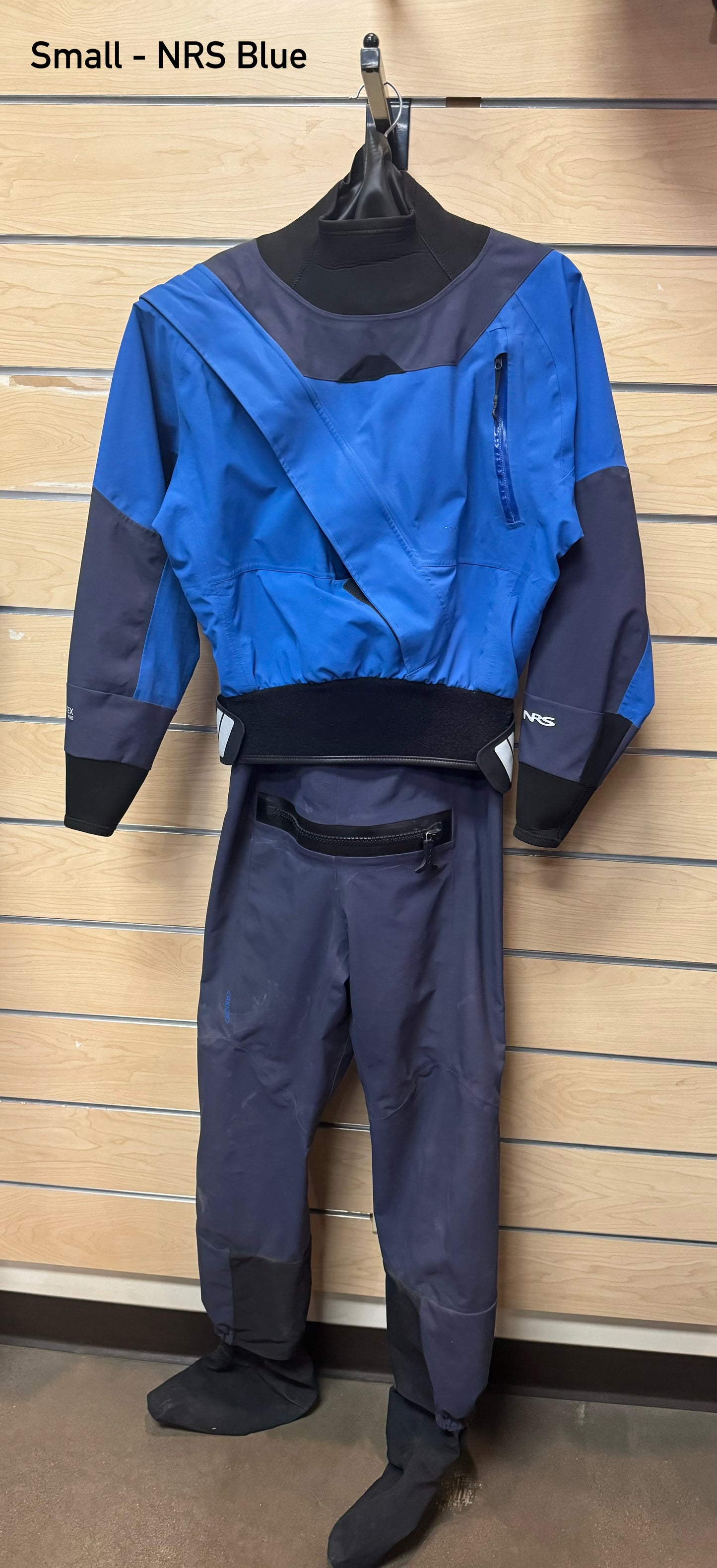 A blue Rental Dry Suit from 4Corners Riversports hanging on a wall.
