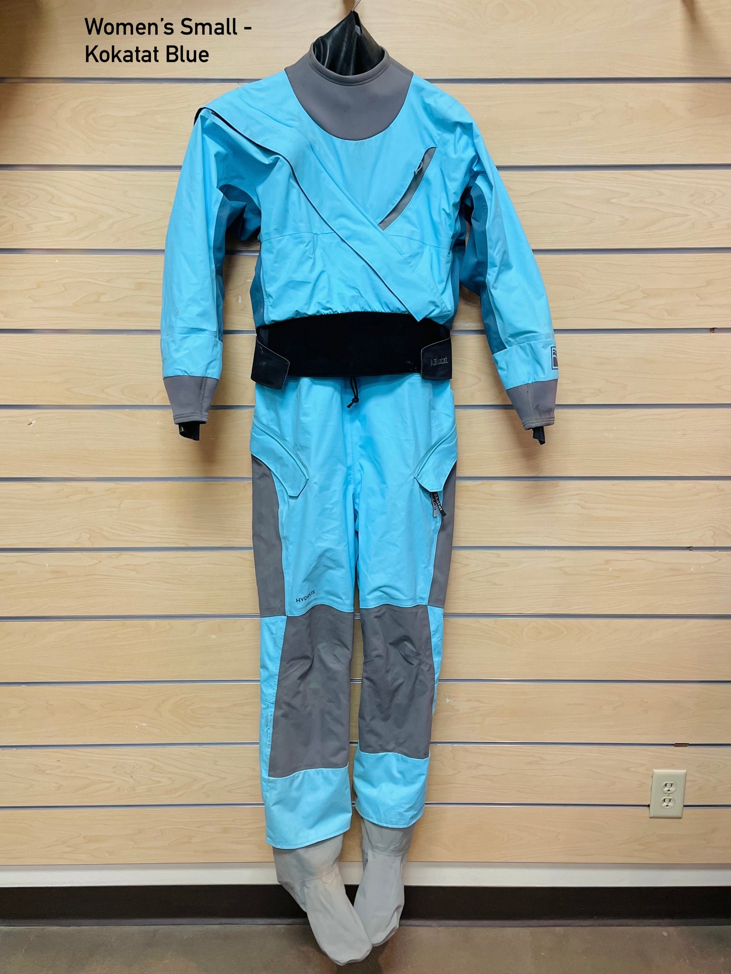 A 4Corners Riversports Rental Dry Suit hanging on a wall, available for shipping.