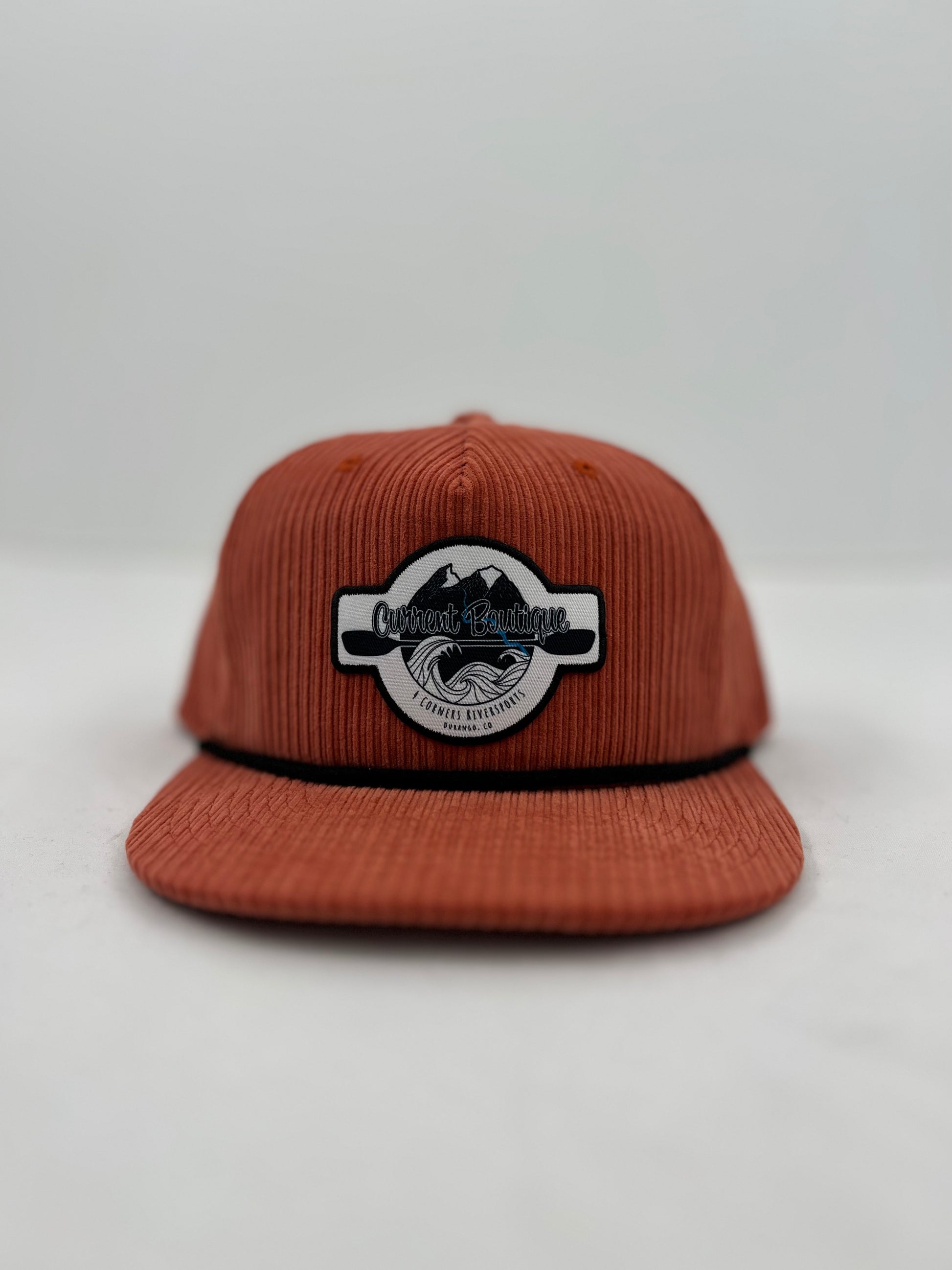 A Current Boutique Cord Pops Hat by Captuer Headwear with a logo on the front, displayed against a neutral background.