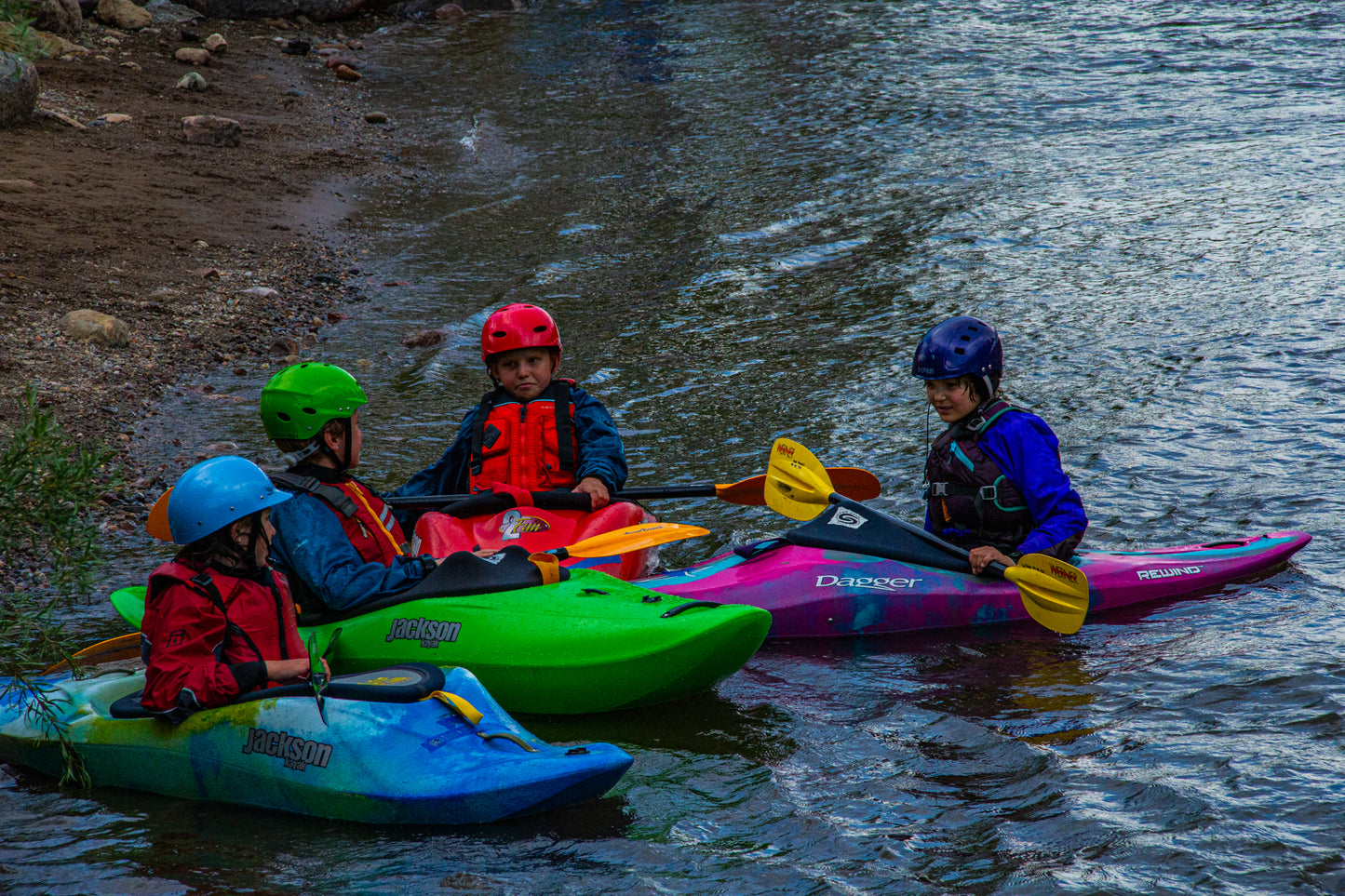 A group of kids taking the Youth Level 1 Kayak Class by 4CRS Paddle School, paddling kayaks on a whitewater river, ensuring their safety.